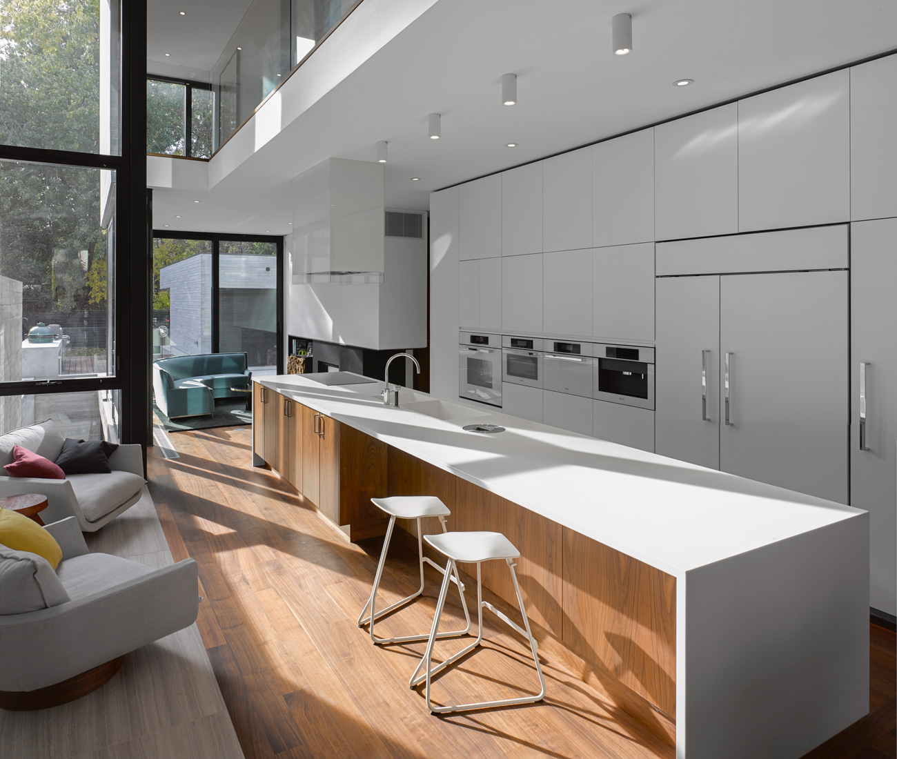 Walnut flooring and built-ins warm the cool interior. Lacquered cabinetry by O’Sullivan Millwork houses Miele’s Brilliant White appliances; the five-metre-long island is topped in Corian. Photo by Ben Rahn /A-Frame.