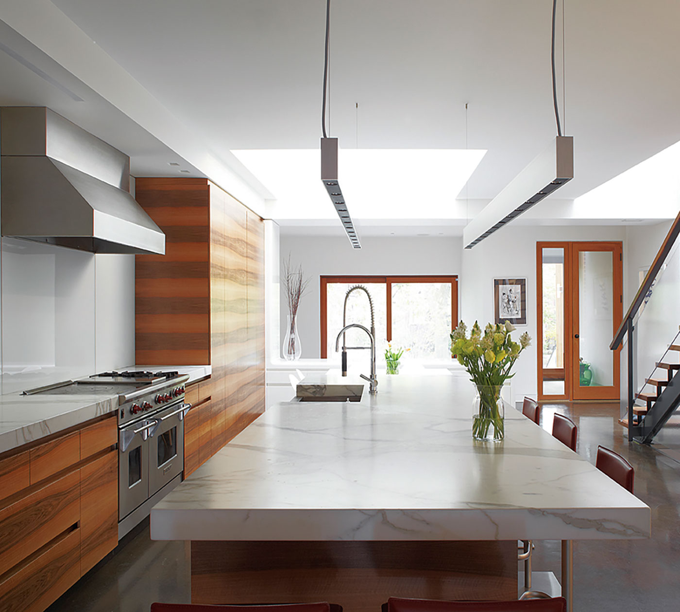 The kitchen’s book-matched wood grain, Carrera marble– topped island and thin suspension lights elongate the space.
