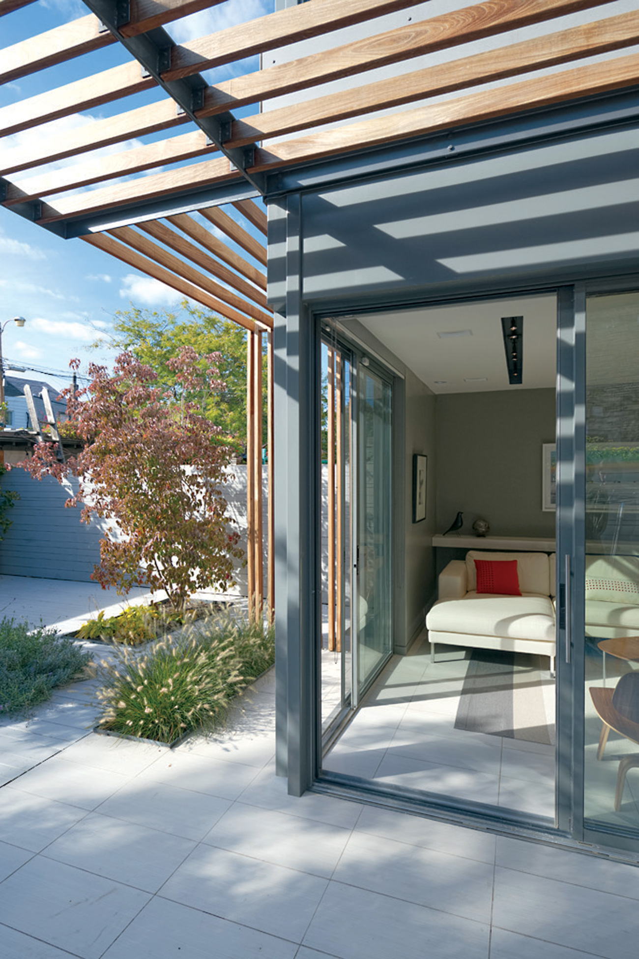 Interior porcelain tile pushes past the sliding doors to the patio. The pergola shades sunken gardens.