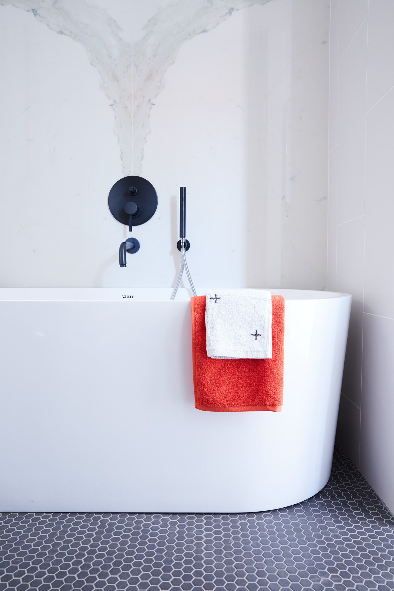 An oval soaker tub by Valley pops against Stone Tile flooring and Ciot wall tile. Towels from CB2 and Drake General Store. Photo by Naomi Finlay.
