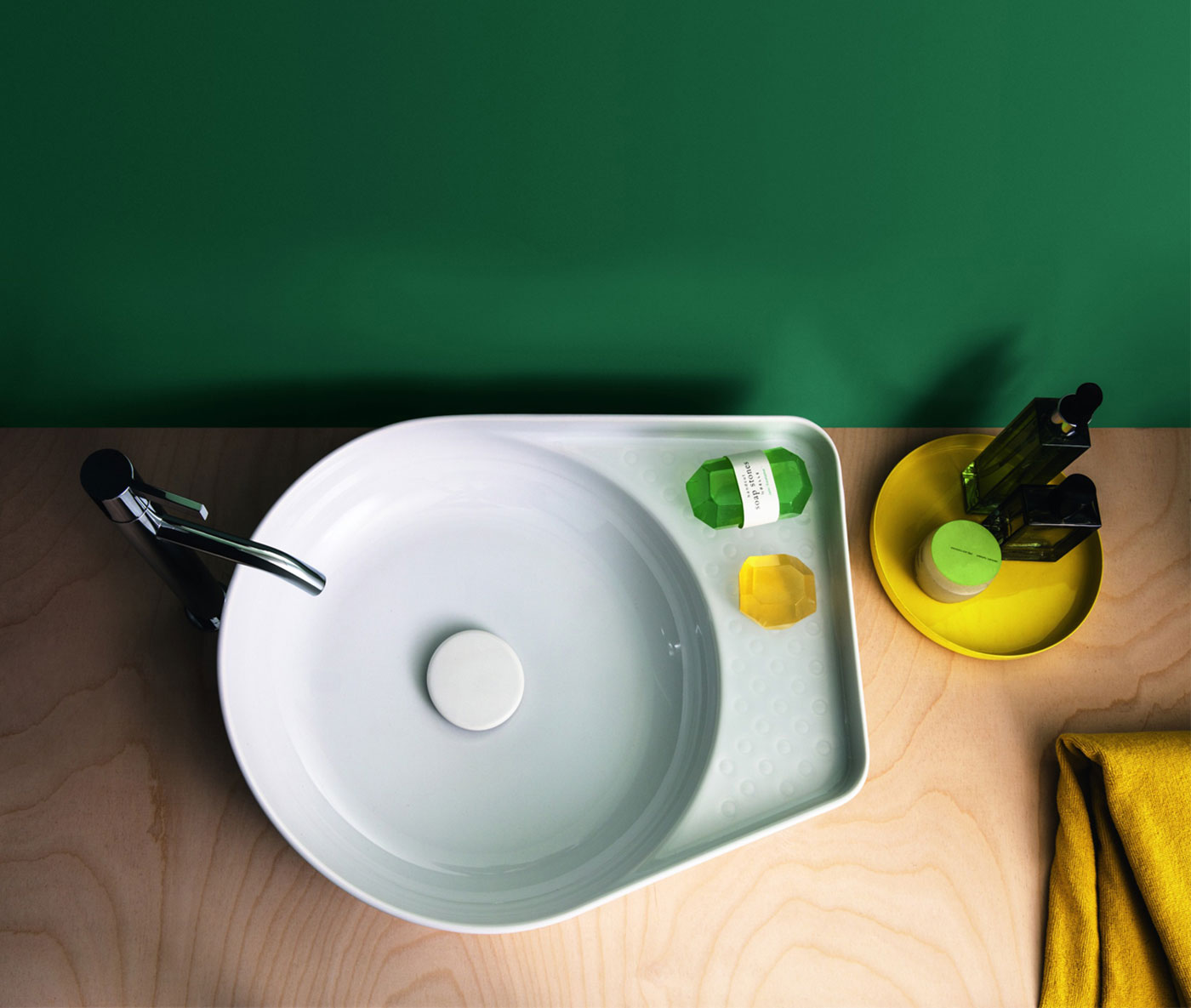 Ceramic Circular Vessel Bathroom Sink against a green background. Soaps are visible in on the counter