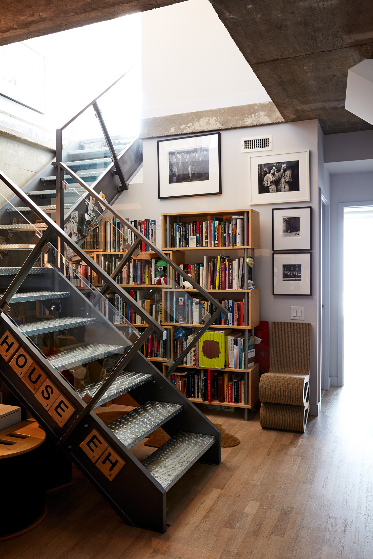 The foyer’s steel staircase rises next to art books on shelving from Urban Mode and Gehry’s cardboard Wiggle side chair for Vitra from ShopAGO.