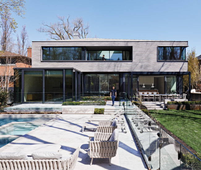 Backyard of minimalist Toronto home designed by AKB Architects. A paved patio with chairs is facing a pool