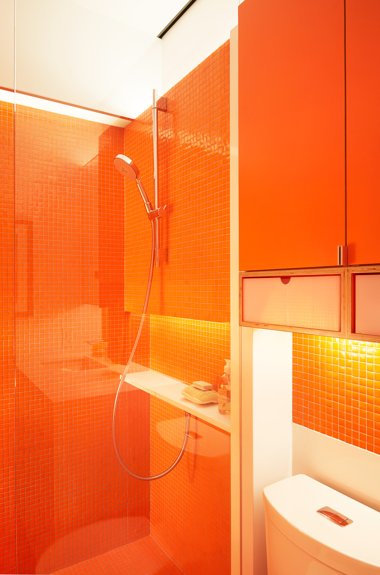 The bathrooms are colour blocked, one in yellow, the other in orange. The designer used miniature molten mosaic tiles from Trend USA in both rooms.