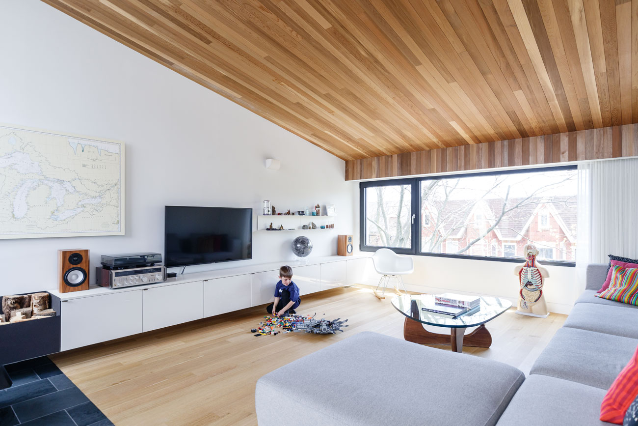 The angled, cedar-clad ceiling is a fitting choice for the third floor living room, a treetop retreat for the family.Sofa, coffee table and Eames chair from Quasi Modo; sconces from YLighting. Photo by Arash Moallemi. 