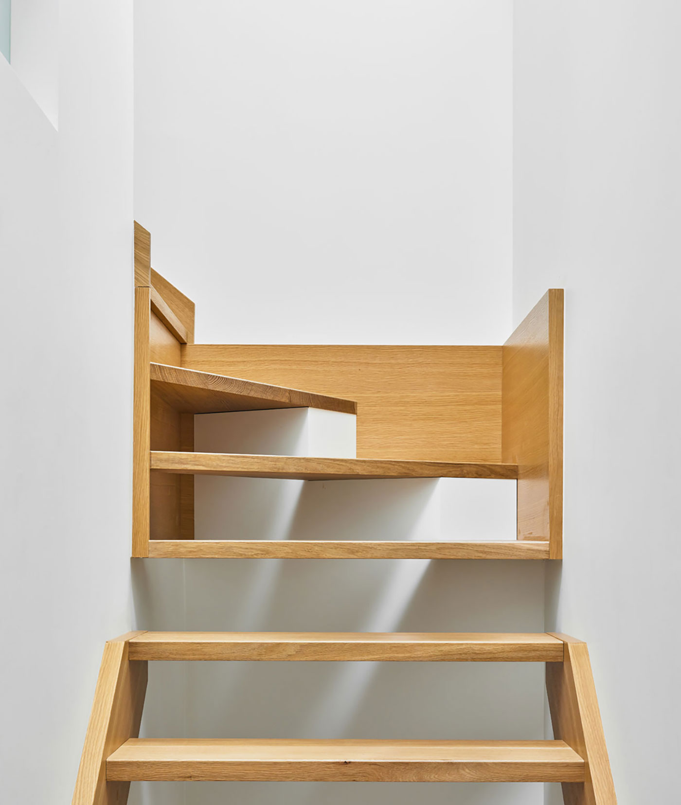 The staircase (built by LaFabrika) spans three storeys and features open white oak treads on concealed brackets.