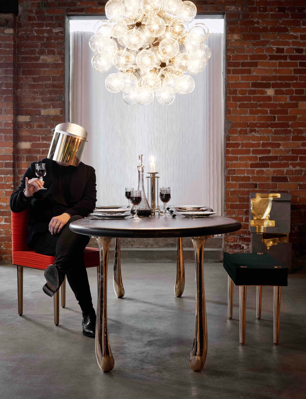 Forrest (masked) is sitting on a chair from Stacklab's Felt collection. The table, featuring oxidized oak top and mirror-polished bronze legs, is from their Jupiter collection. The light fixture is an original Castiglioni purchased from Porch Modern.