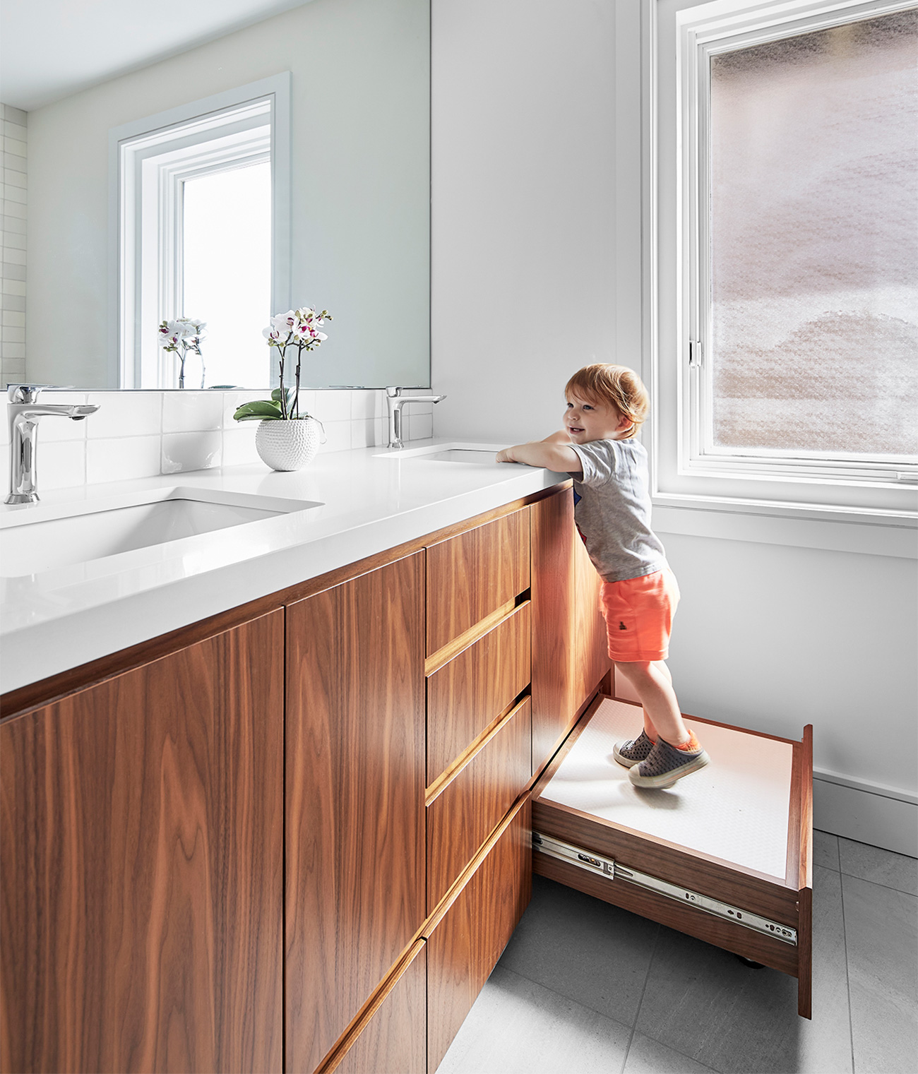 Because the homeowners are frequently visited by the grandkids, Myers updated a family bathroom, complete with stowable step stool. Walnut cabinetry and custom vanity by Millworx; Artemide sconces.