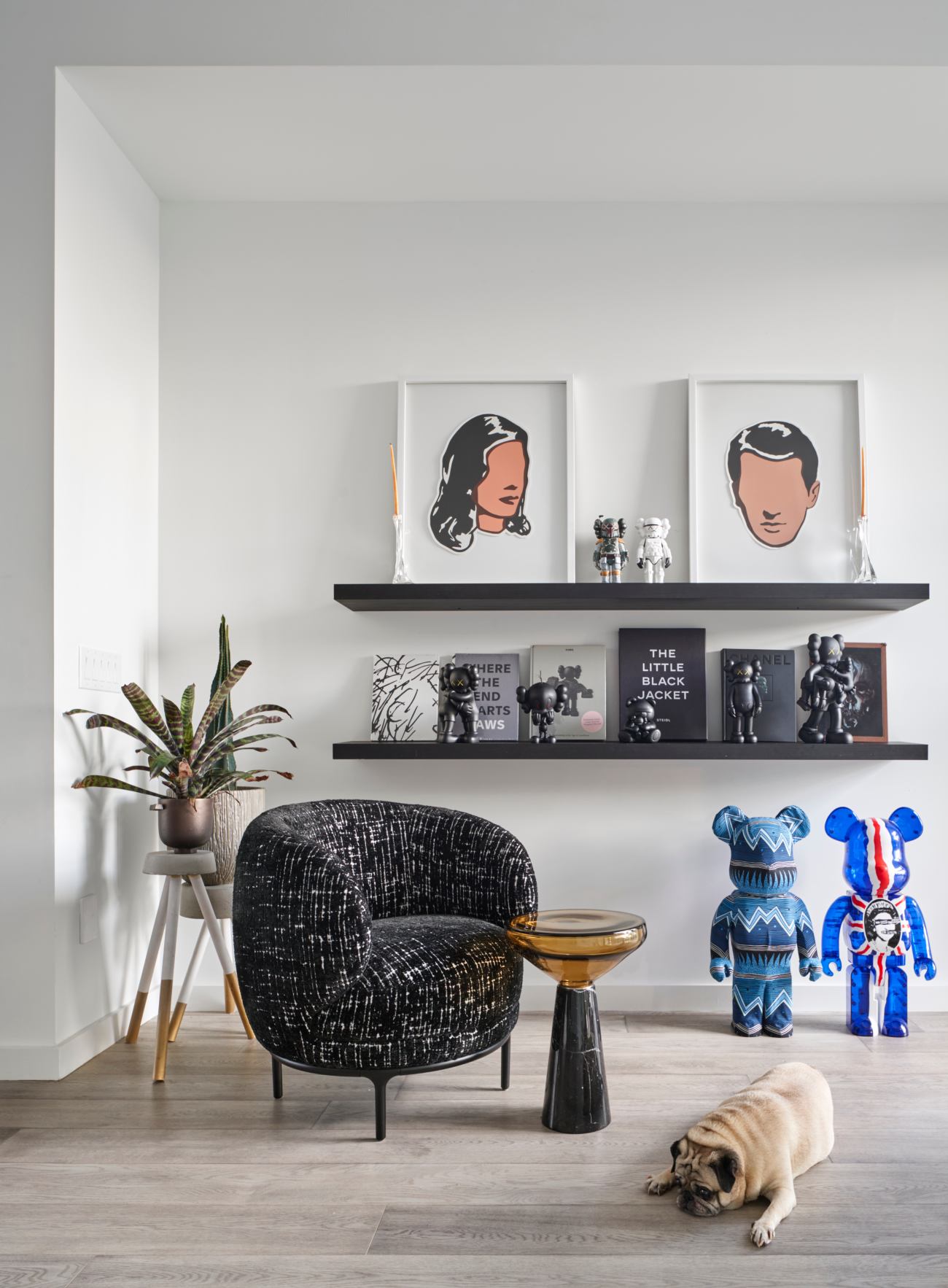 The lounge chair, from Avenue Road, is by Jamie Hayon. The side table, from Klaus, is by Stephen Veit. The prints, by Adriana Oliver, share shelf space with Kaws figurines. On the floor, Stussy 1000% and Sex Pistol 1000% Bearbrick figurines.