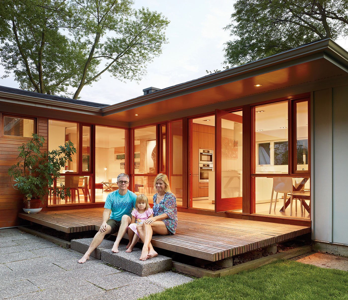 Family of 3 people (dad, mom and daughter) sitting on a wooden deck outside a renovated home in Etobicoke
