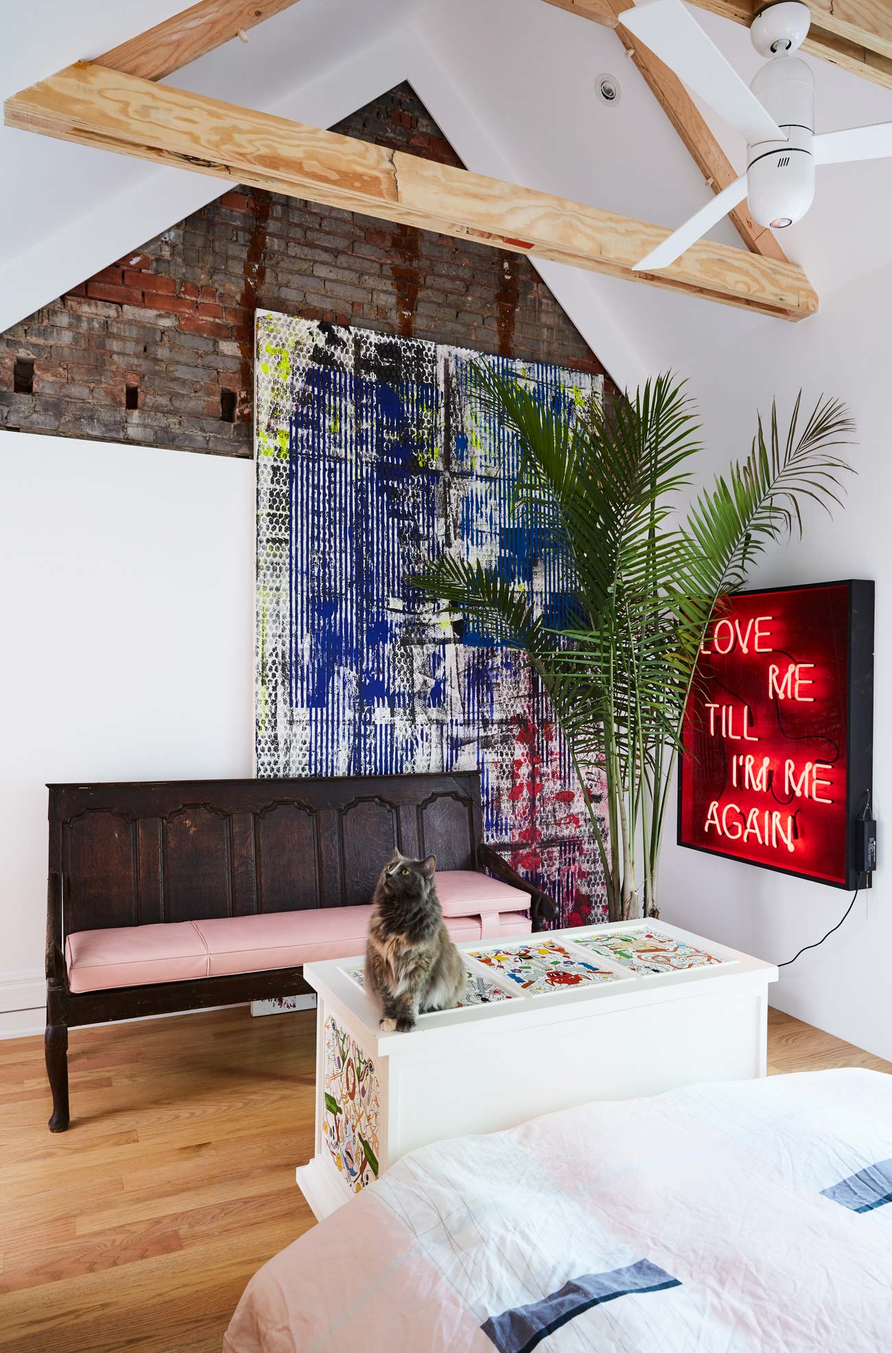 Bedroom with cathedral ceiling and art on the walls. A cat is sitting on a piece of furniture 