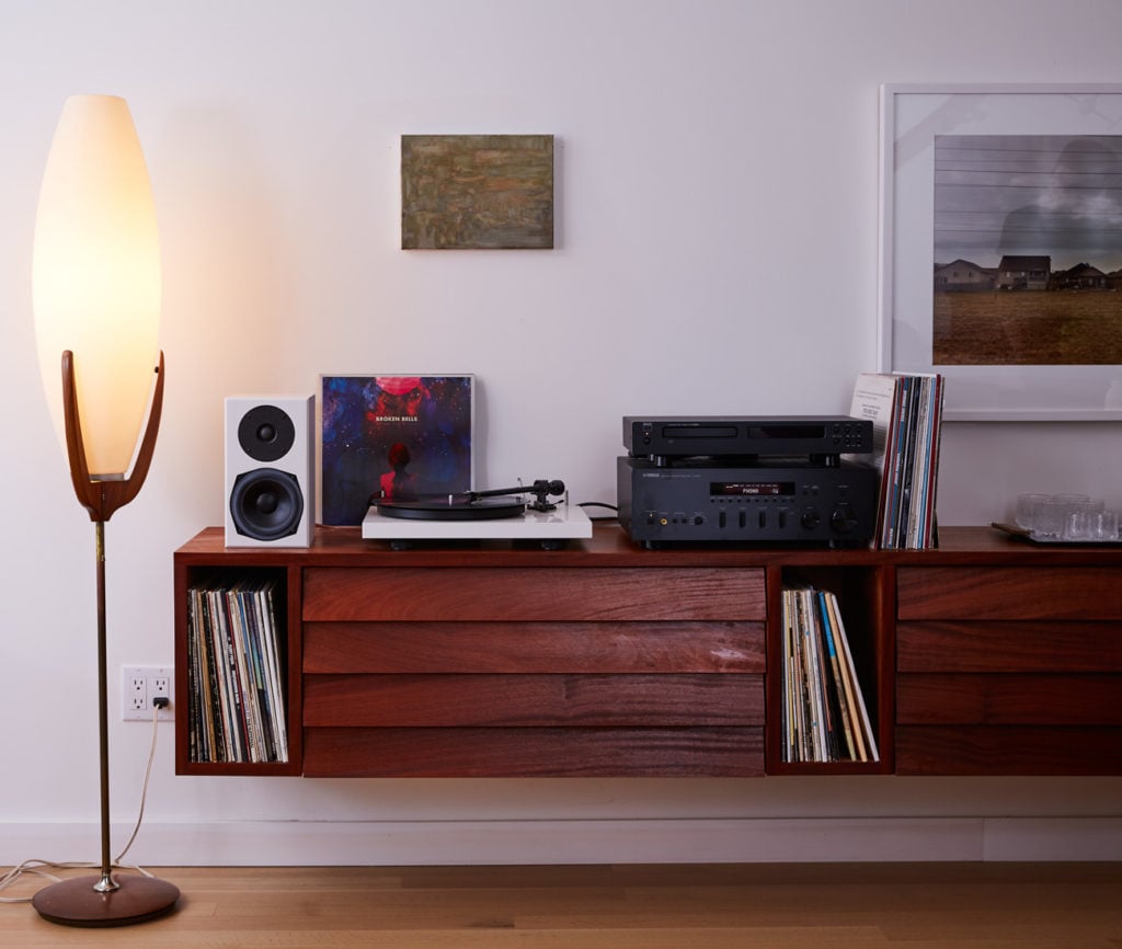 Wall-mounted cabinet for vinyl records highlights custom millwork projects, featuring a turntable and vintage lamp.