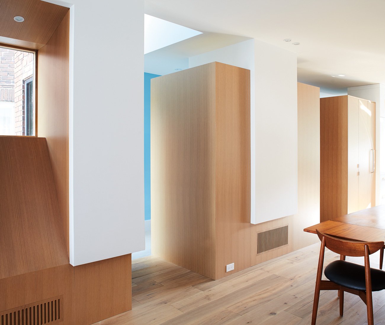 White oak volumes separating hallway and kitchen, concealing storage in a geometric design, Little Italy Toronto renovation.