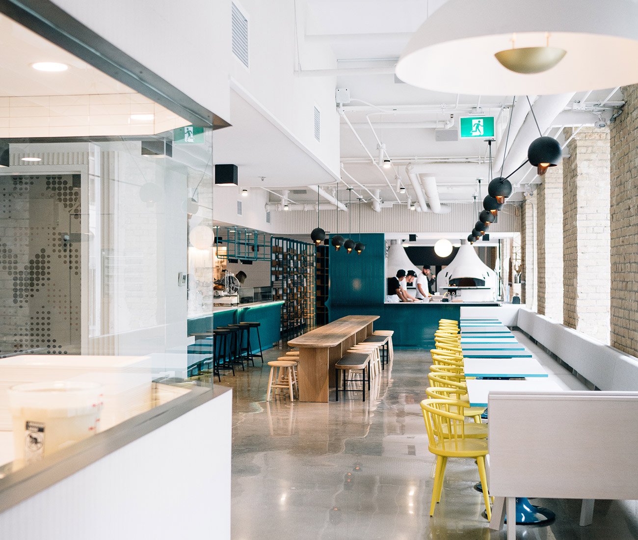 Interior view of General Assembly showcasing the communal table and stylish decor. The pizza ovens are visible in background. Toronto Design Restaurant
