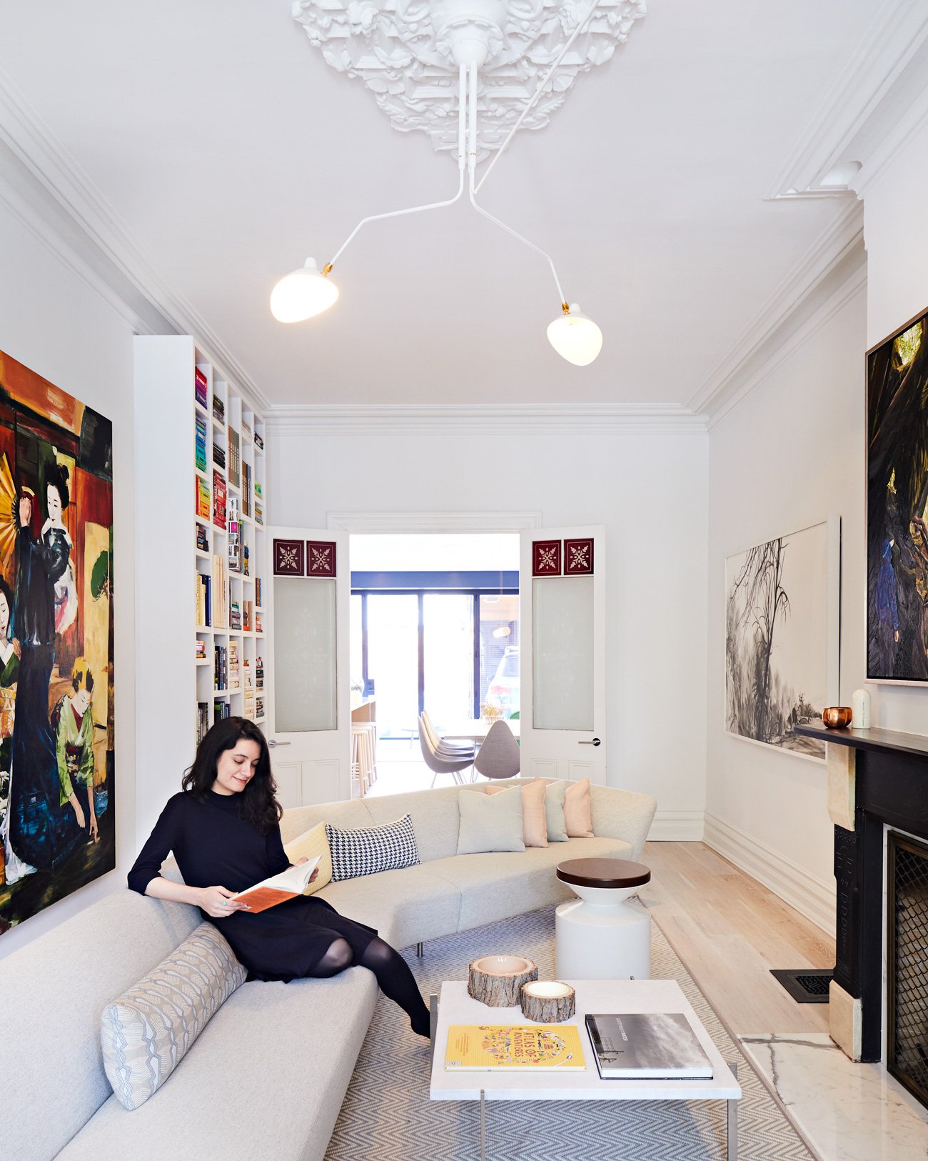 Cabbagetown Victorian Alison Milne Design Toronto Modern Home Young lady seating on a living room sofa reading a book. Arts is filling the walls