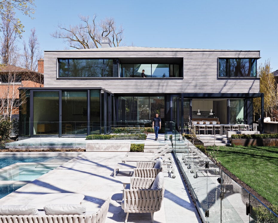 Backyard of minimalist Toronto home designed by AKB Architects. A paved patio with chairs is facing a pool