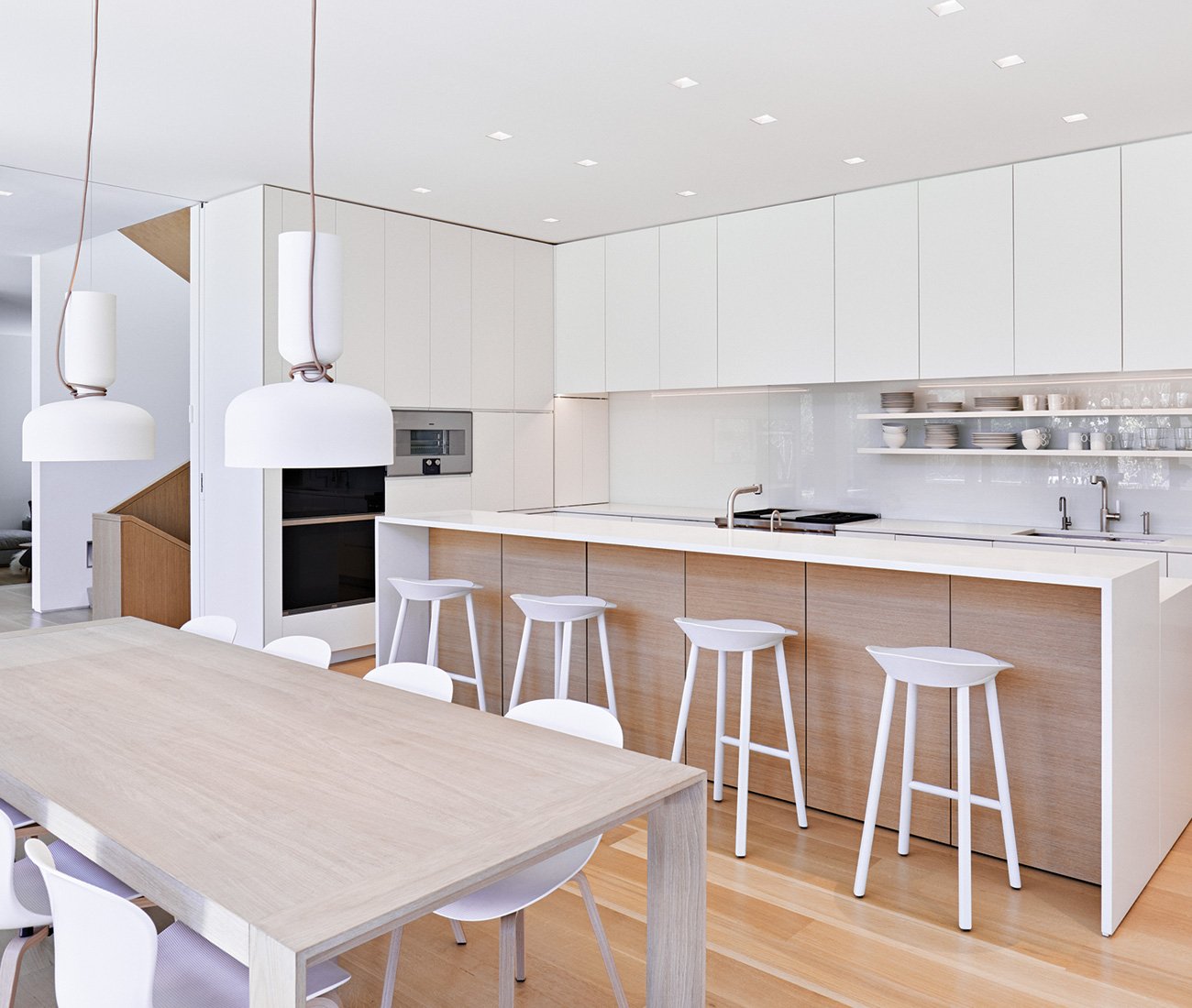 Modern dual-tone kitchen featuring white and wood laminate cabinets extending to the ceiling, a long island, a dining table, and stylish light pendants.