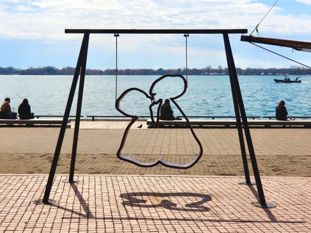 A swinging sculpture of two connected silhouettes facing lake ontario.