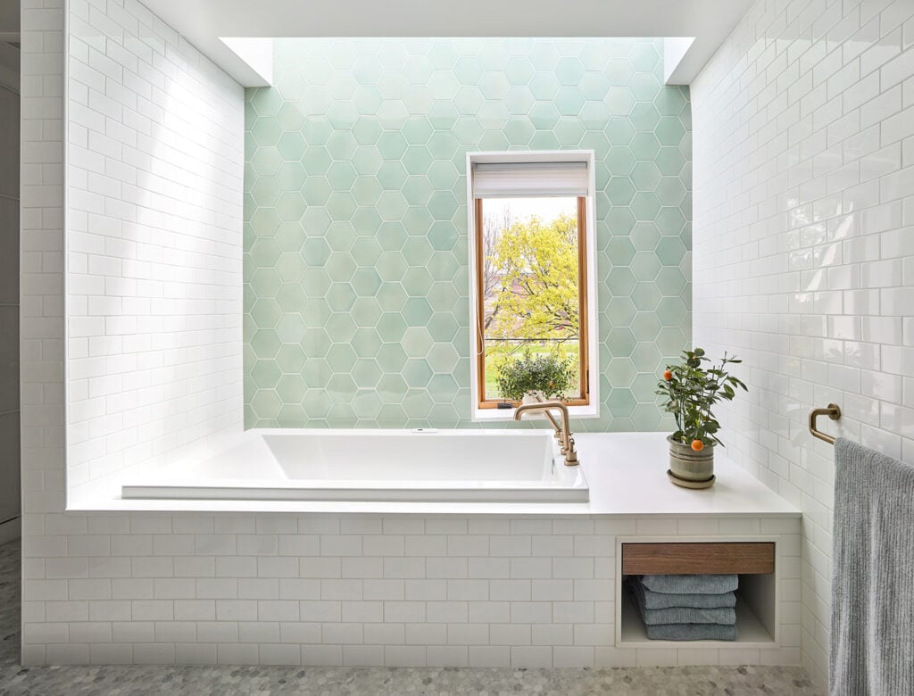 A sage green tiled wall in the bathroom above a white bathtub at Ravina House